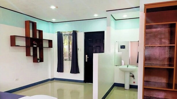 A hotel room with a bed, a small bedside table, a mirror, a wardrobe, and a bathroom with a sink and toilet. - EC Hotel near Laoag Airport (Laoag)