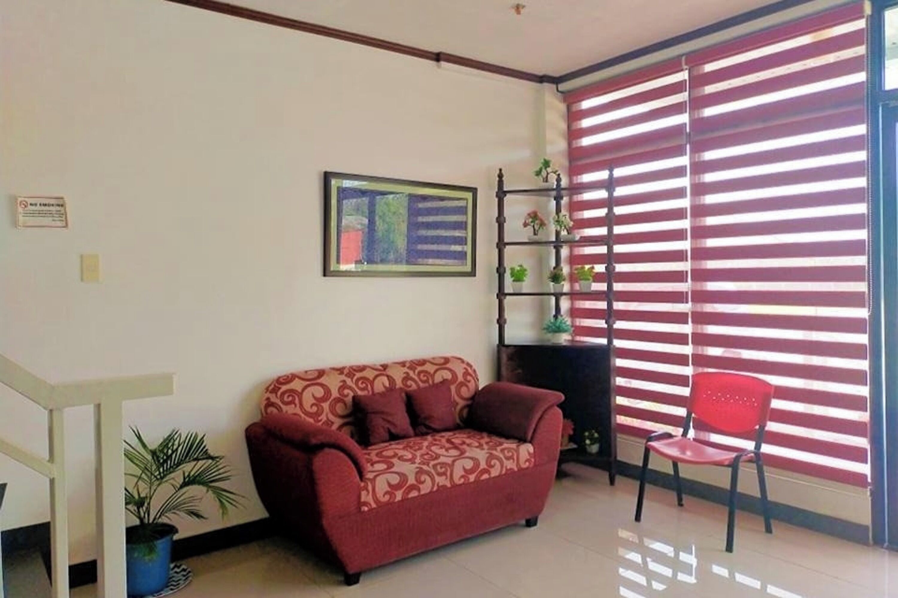 A living room with a red sofa, a red chair, a staircase, and a window with red blinds.