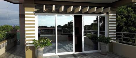 A covered outdoor area with a glass door entrance, potted plants, and a tiled floor.