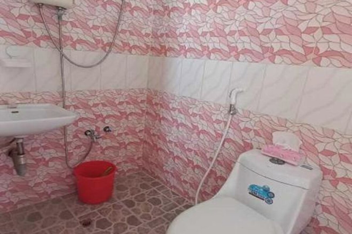 A bathroom with a white sink, a red bucket, a toilet with a blue sticker, and patterned walls.