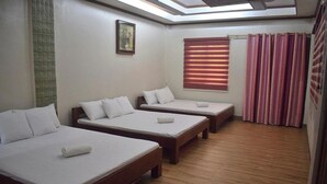Una habitación de hotel con tres camas individuales, una ventana con persianas y un tragaluz.