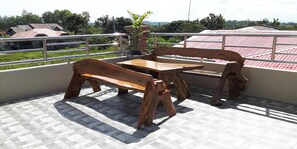 A balcony with a wooden table and benches, a view of houses, and a metal railing. - FNT Transient House near Hundred Islands (Alaminos)