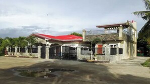 Una casa de dos pisos con techo rojo, entrada protegida por una reja y un pequeño camino de acceso.