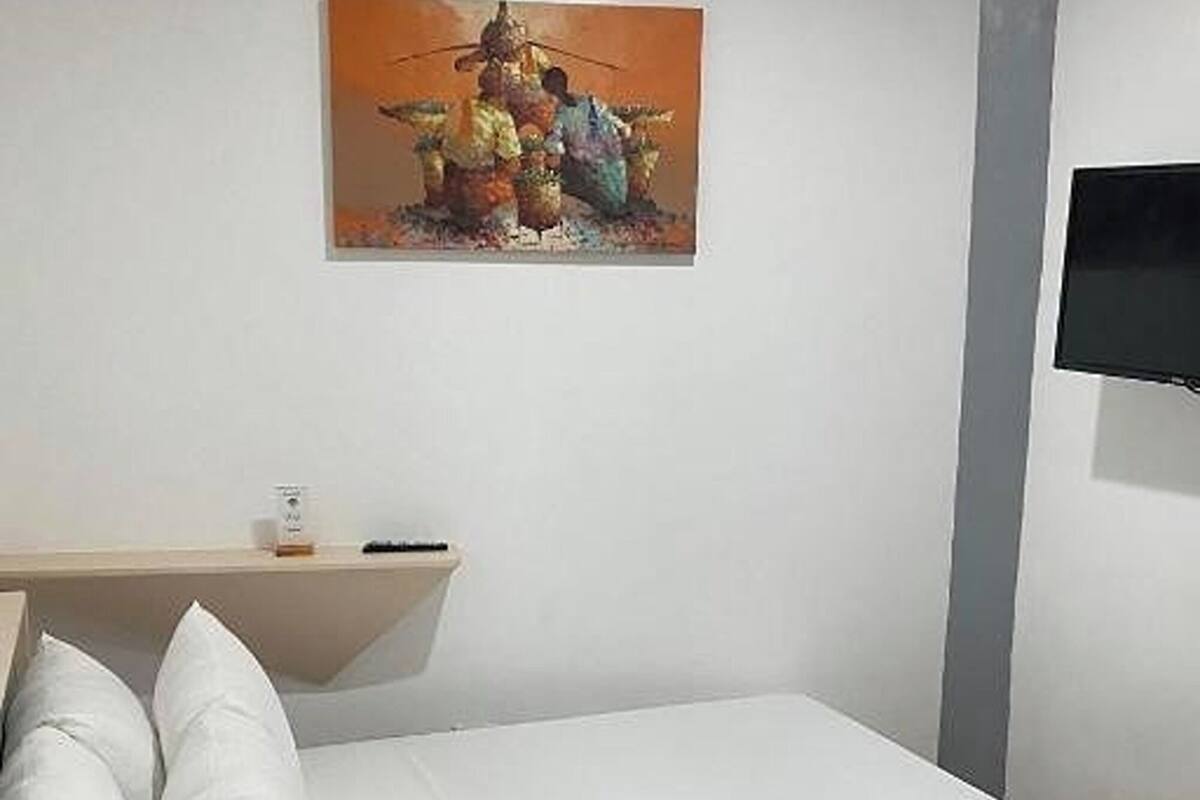 Une chambre avec un lit, un tableau accroché au mur, un téléviseur fixé au mur et une petite table avec une télécommande.