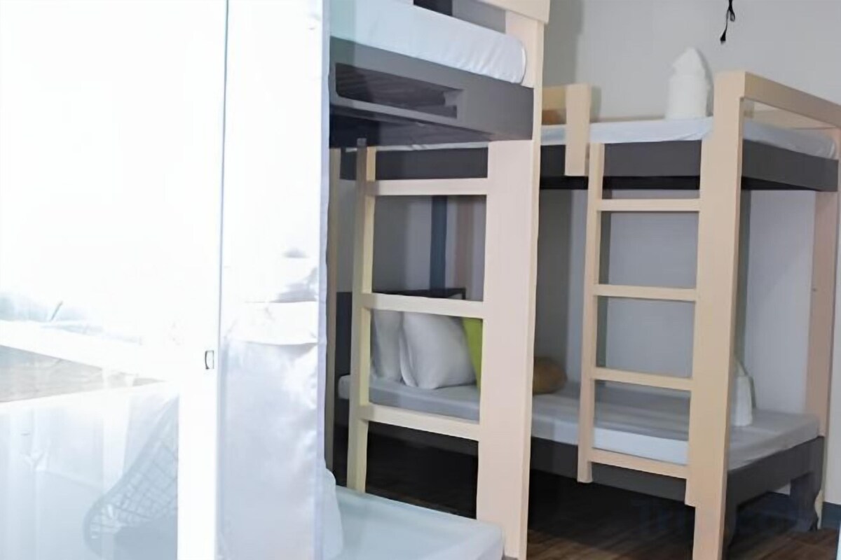 A bunk bed with a white mattress and pillows, a wooden frame, and a small shelf.