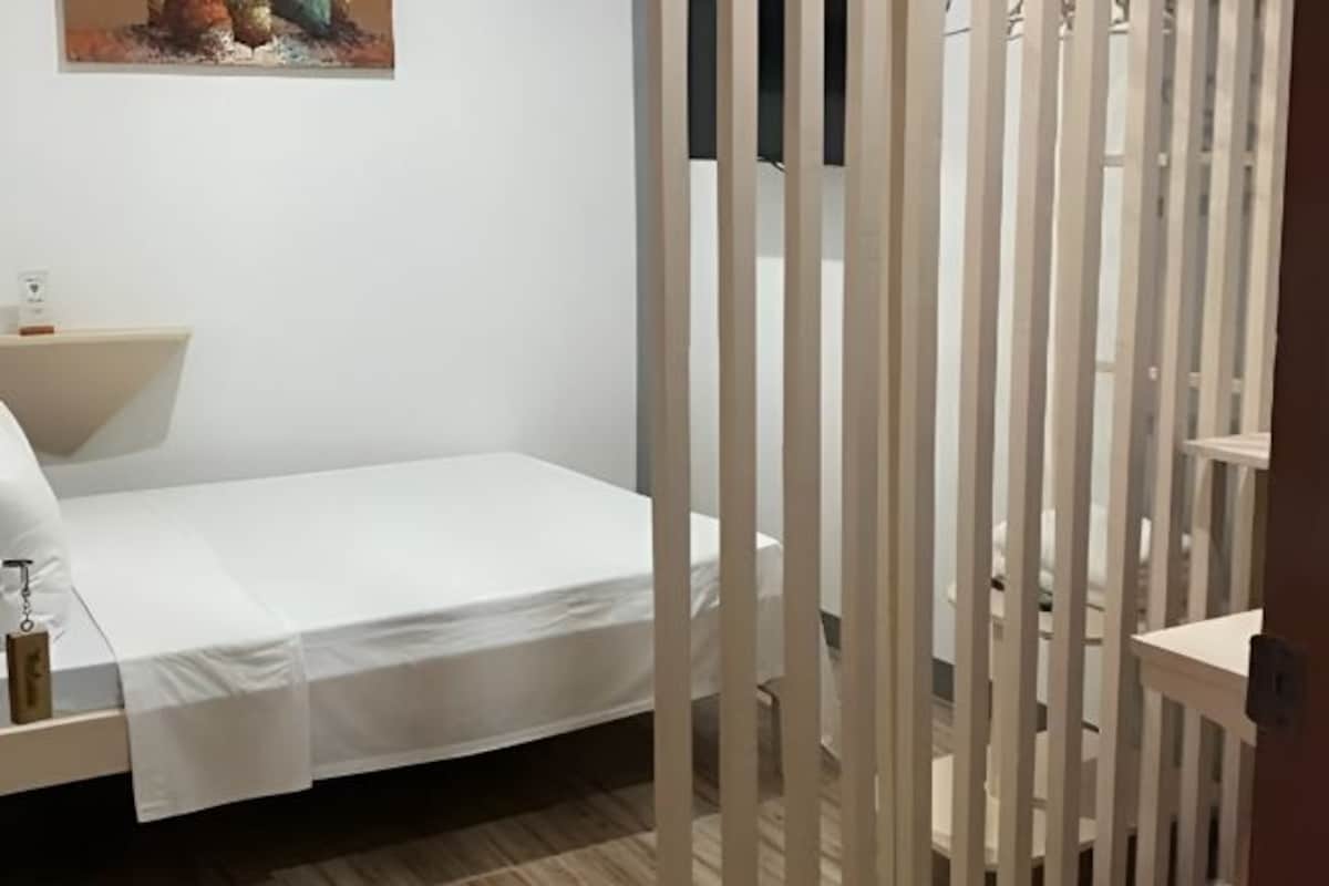 A bedroom with a single bed, a bedside table, and a wall-mounted painting.