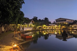Un hôtel paisible situé au bord d’un lac, avec un pont qui se reflète dans l’eau, créant un effet miroir sur les bâtiments et les arbres.