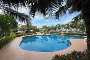 Ein Pool mit geschwungener Kante, umgeben von einer gefliesten Terrasse und Palmen.