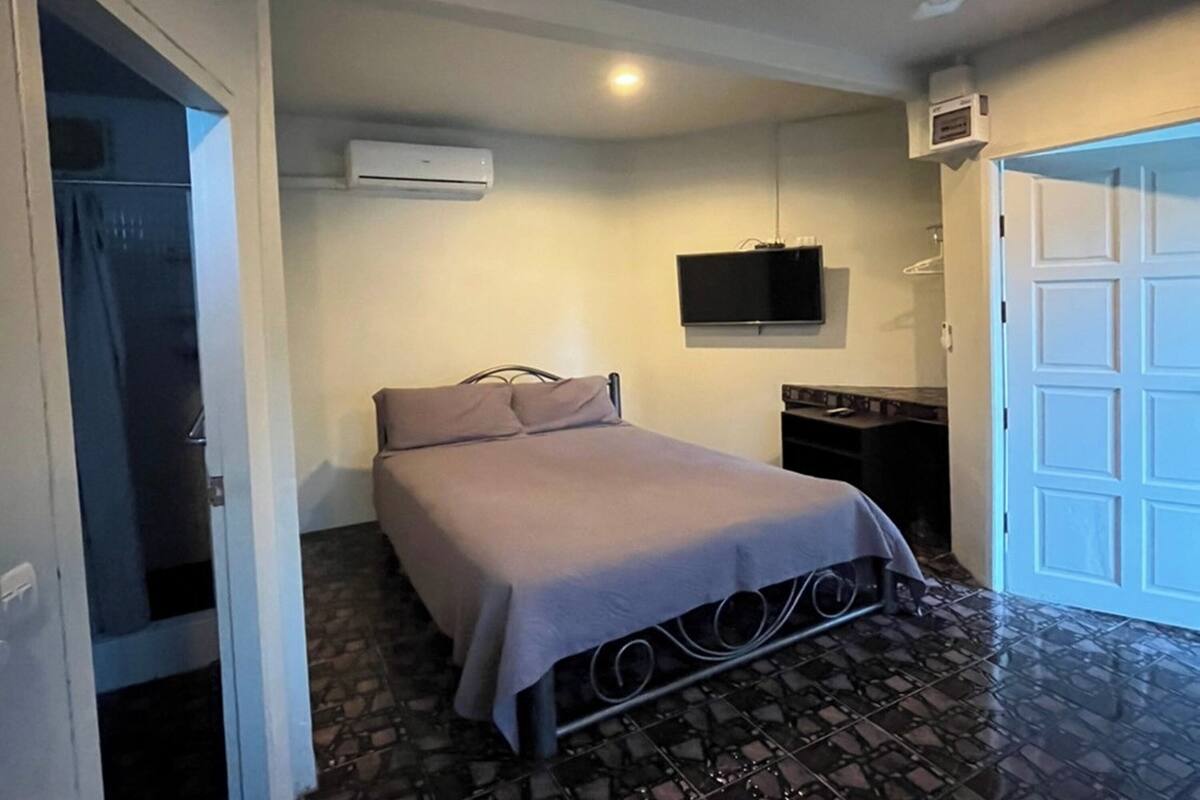 Une chambre à coucher comprenant un lit, un climatiseur, un téléviseur et un sol carrelé.