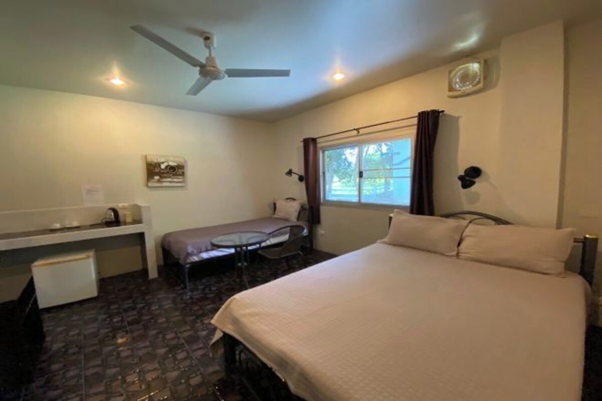 Une chambre d’hôtel équipée d’un lit, d’un bureau, d’une chaise, d’une petite table et d’un ventilateur de plafond.