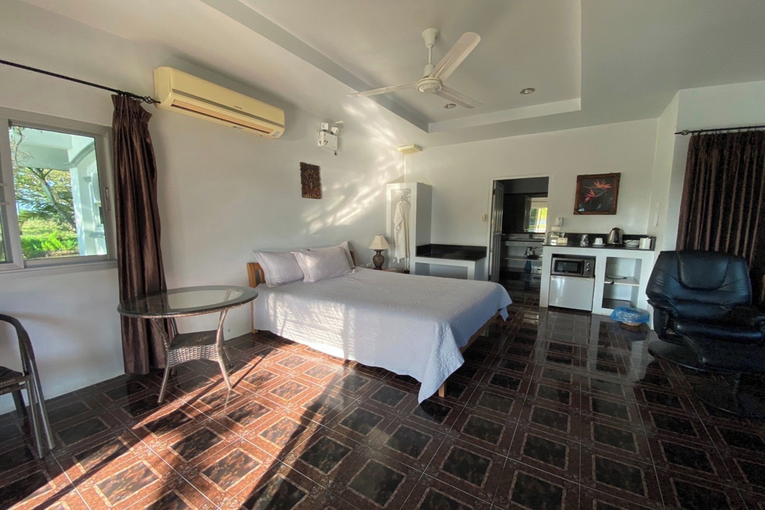 Une chambre d’hôtel comprenant un lit, une petite table, une chaise, un ventilateur de plafond, un appareil de climatisation, un coin cuisine et une vue sur la verdure.