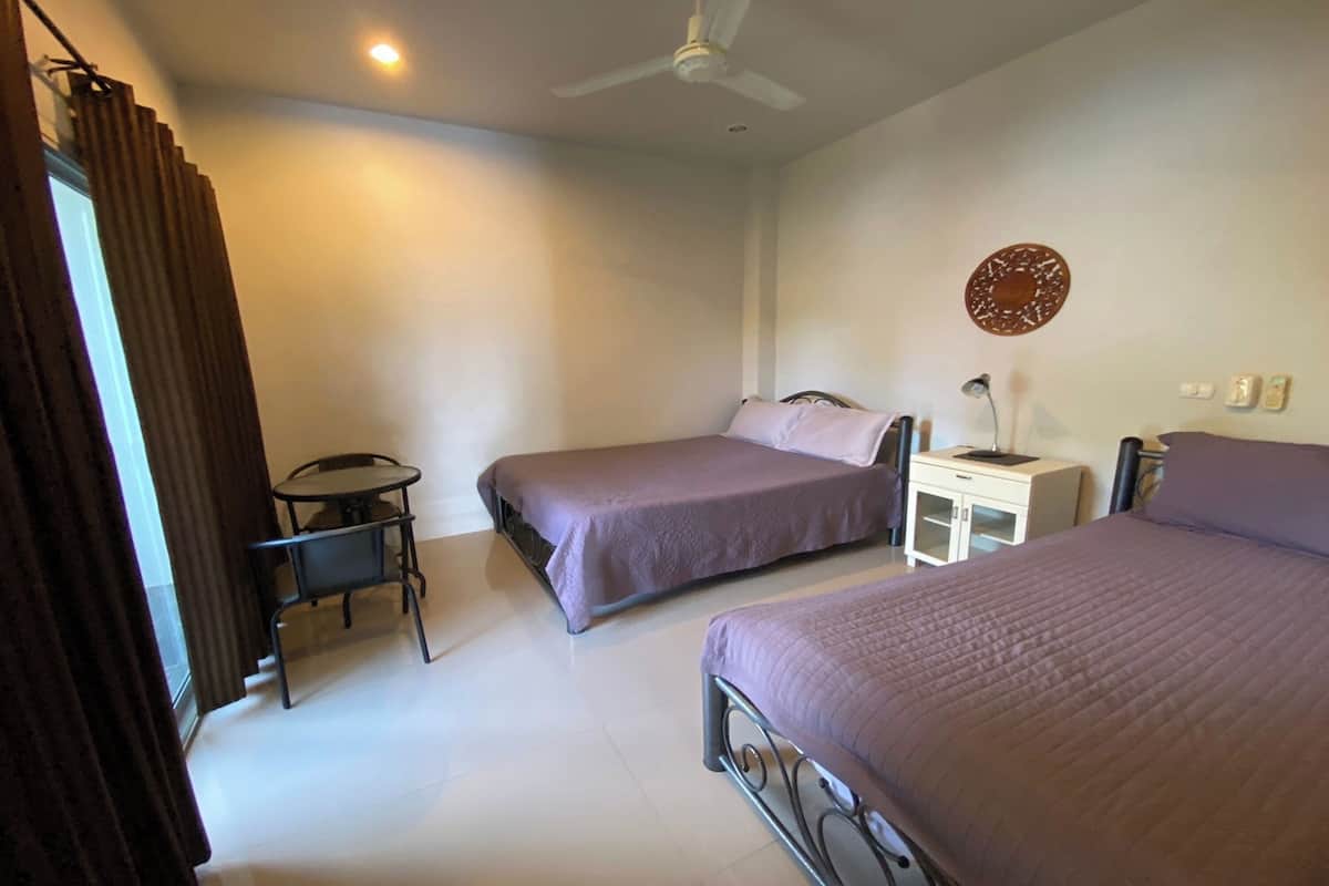 Une chambre d’hôtel avec deux lits, une petite table, une chaise, un bureau et un ventilateur de plafond.