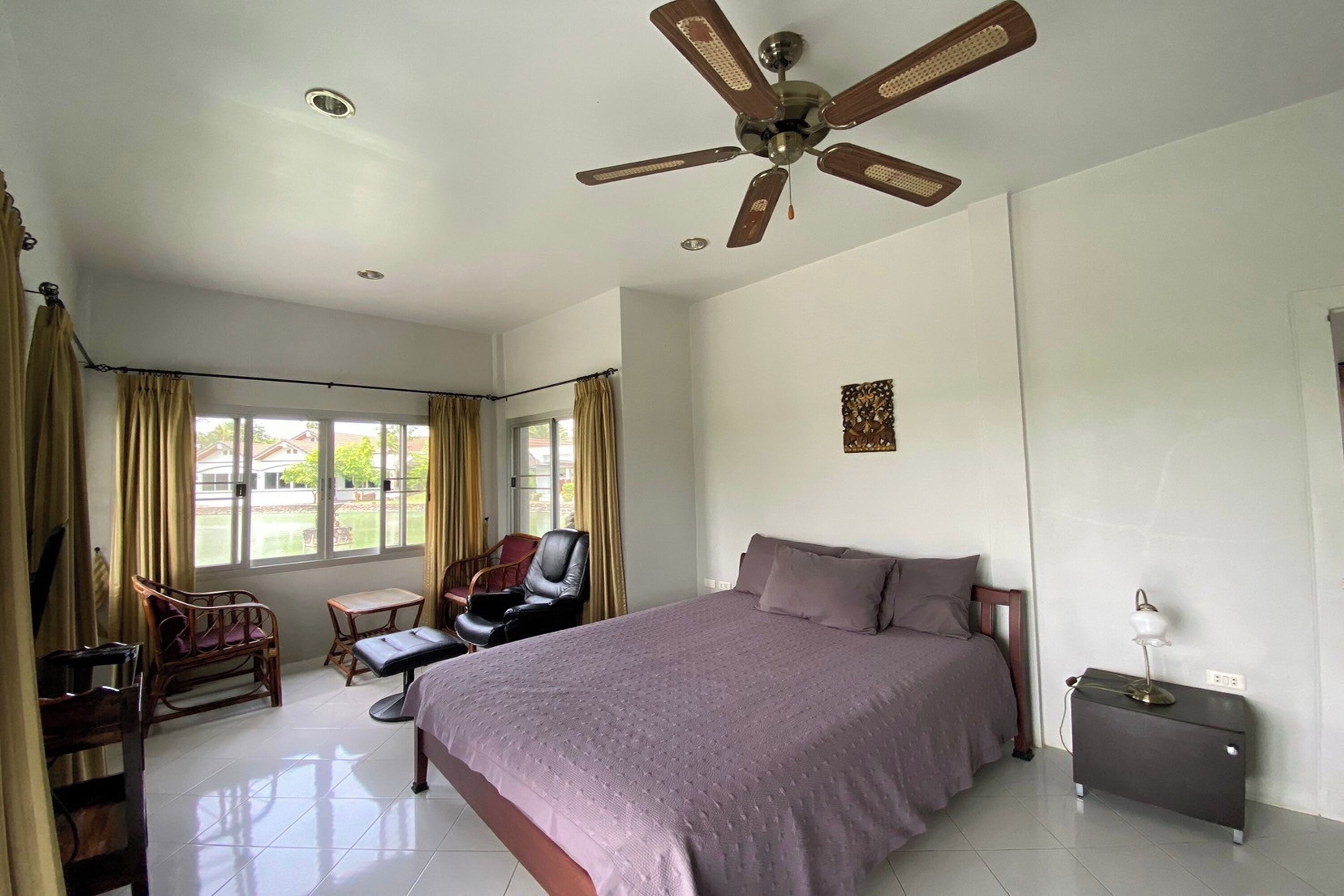 A bedroom with a bed, a desk, a chair, a ceiling fan, and a window with curtains.
