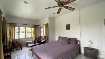 A bedroom with a bed, a desk, a chair, a ceiling fan, and a window with curtains.