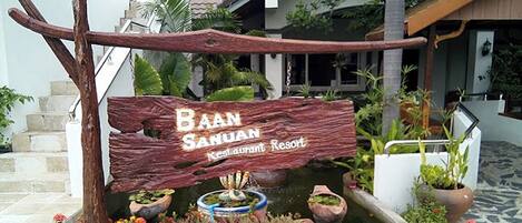 A wooden sign for Baan Sahuan Restaurant Resort with a small pond and potted plants.