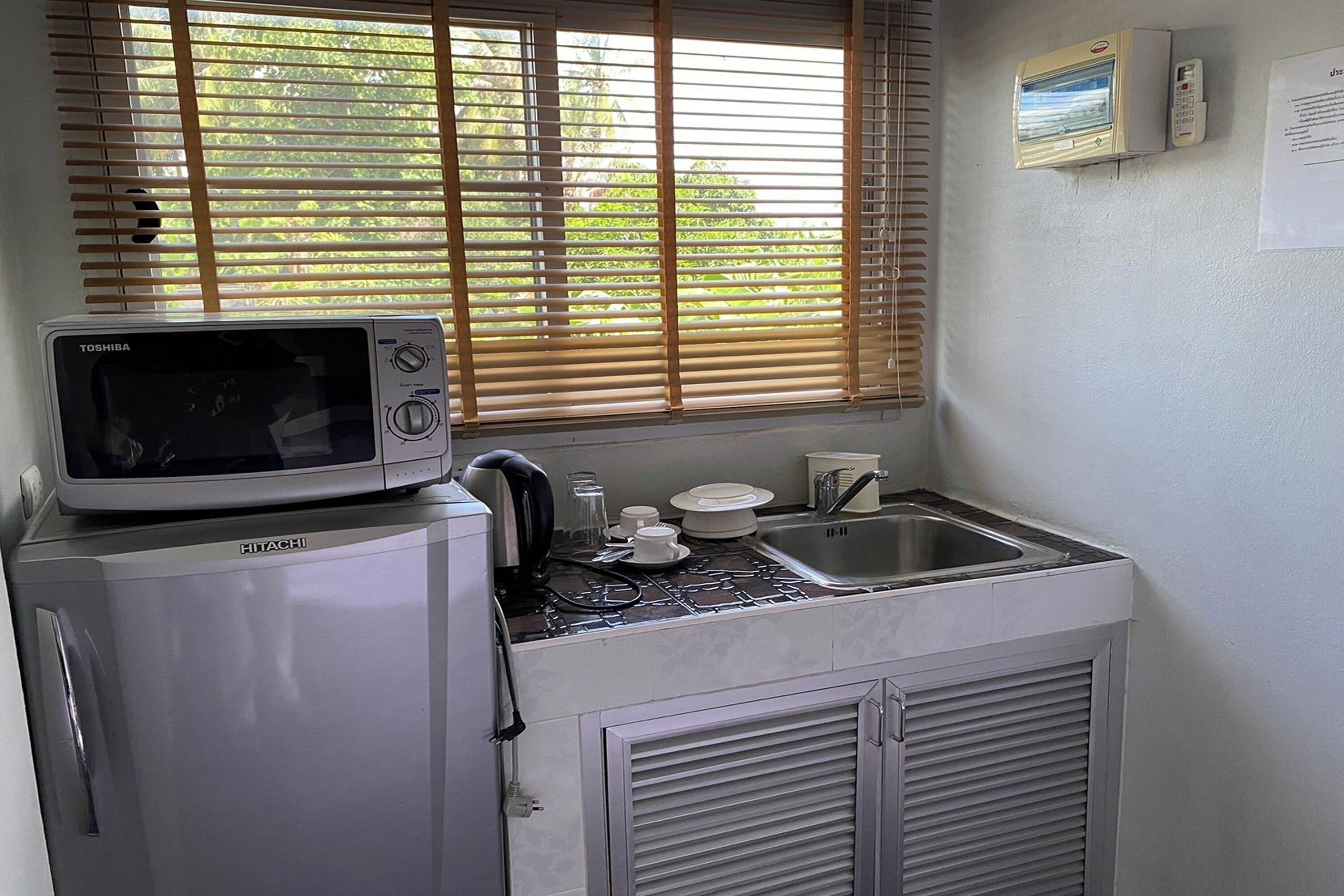 Una cocina compacta con microondas integrado, un lavamanos pequeño y una ventana con persianas.