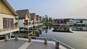 A riverside hotel with a reflection in the water, a covered outdoor seating area, and a modern building with a sloped roof. - Burichan Resort (Chanthaburi)