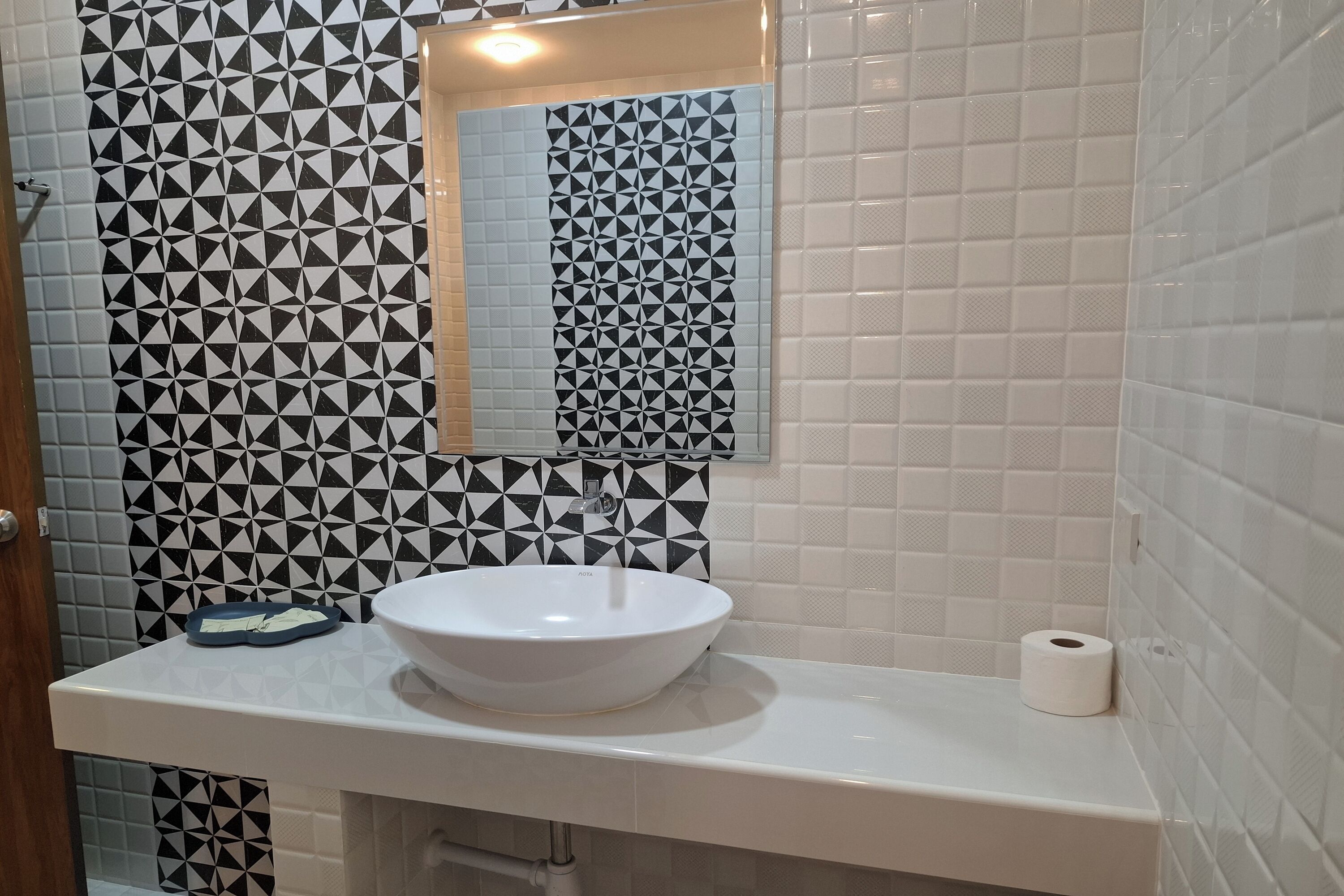 A bathroom with a white sink, a mirror, and patterned tiles on the walls.