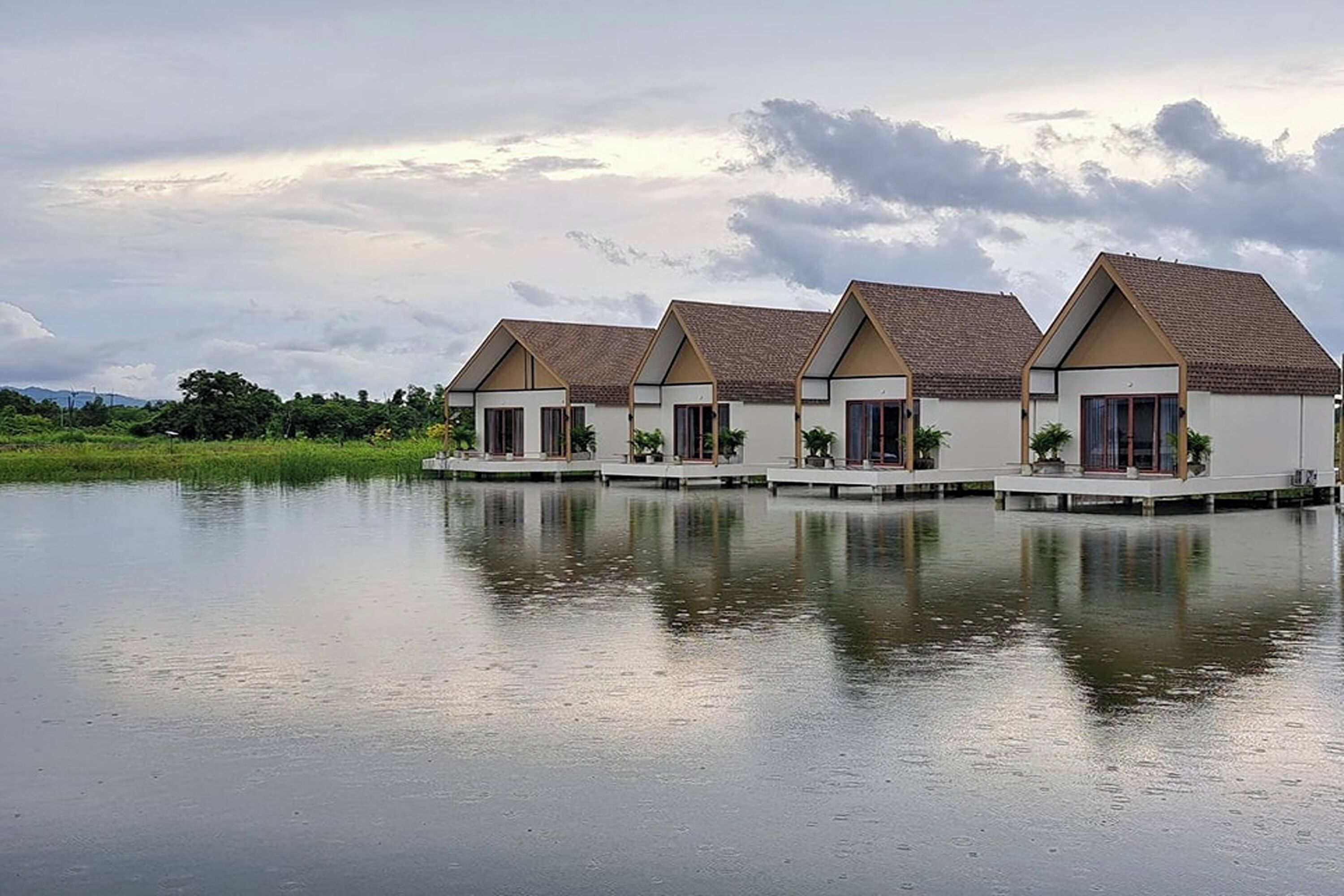 A row of white buildings with brown roofs, each with a balcony, situated by a calm body of water.
