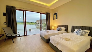 A hotel room with two beds, a chair, a large window with a view of a body of water, and a painting on the wall. - Burichan Resort (Chanthaburi)