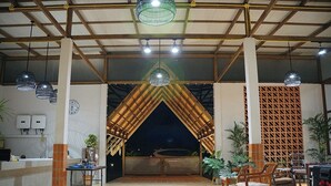 A spacious indoor area with a tiled floor, wooden beams, and hanging pendant lights. There are tables and chairs arranged for dining or socializing. - Burichan Resort (Chanthaburi)