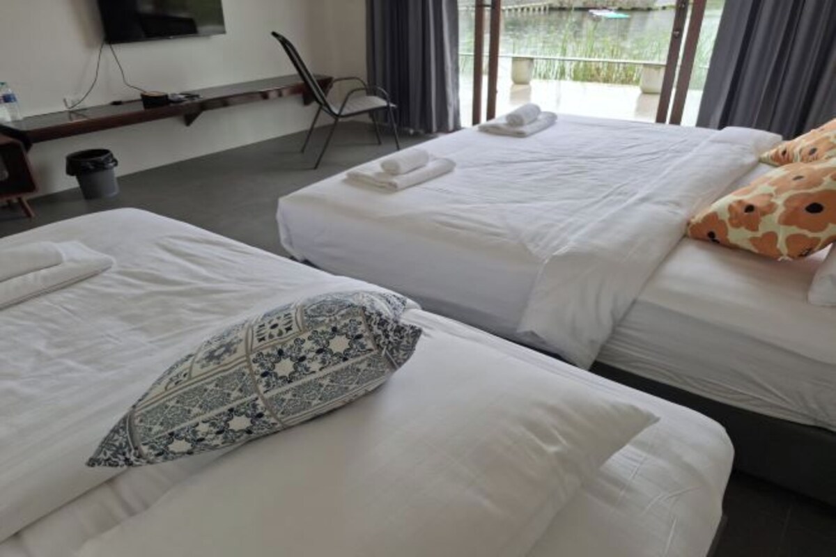 A hotel room with two beds, each with white linens and decorative pillows. There is a chair and a small table with a water bottle and a trash bin.