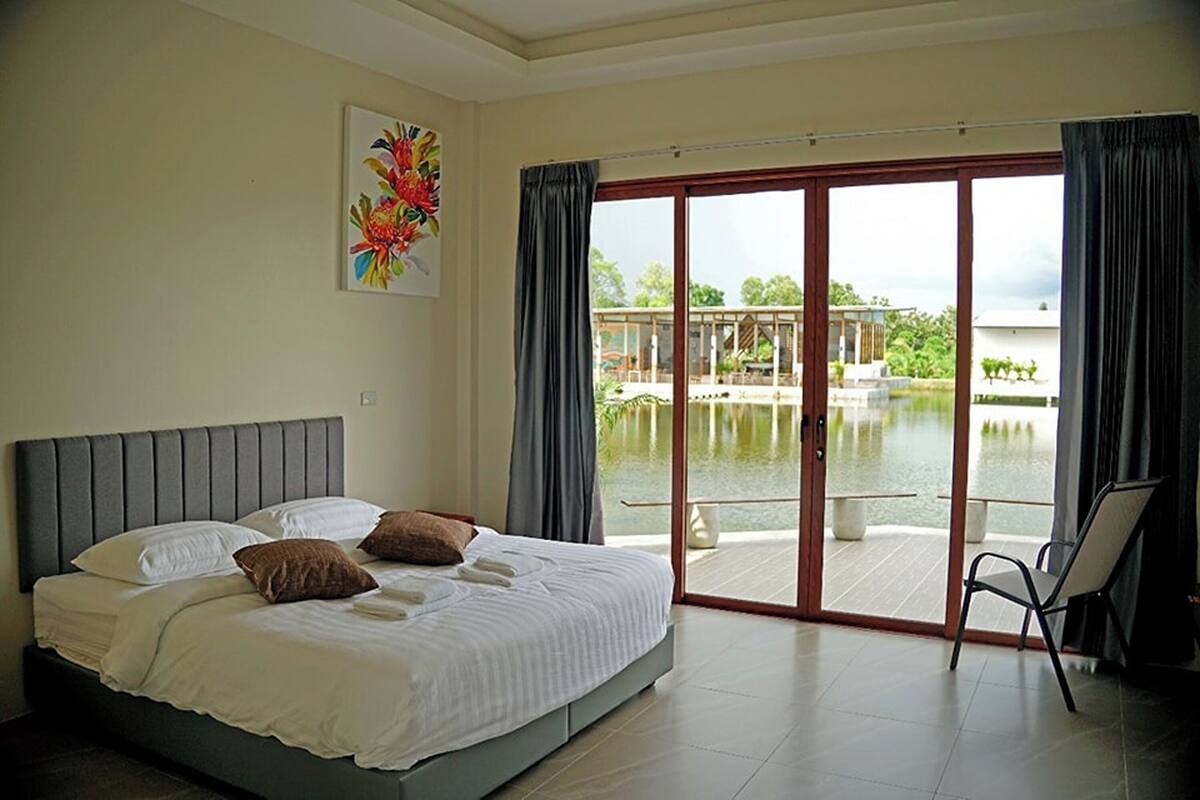 Ein Schlafzimmer mit Bett, Sessel und Blick auf Pool und Garten.