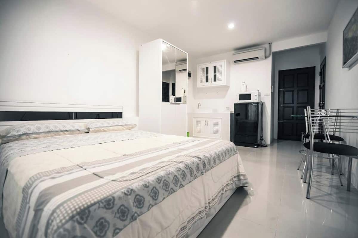 A modern bedroom with a large bed, a built-in wardrobe, a mirror, and a kitchenette area with a microwave and sink.