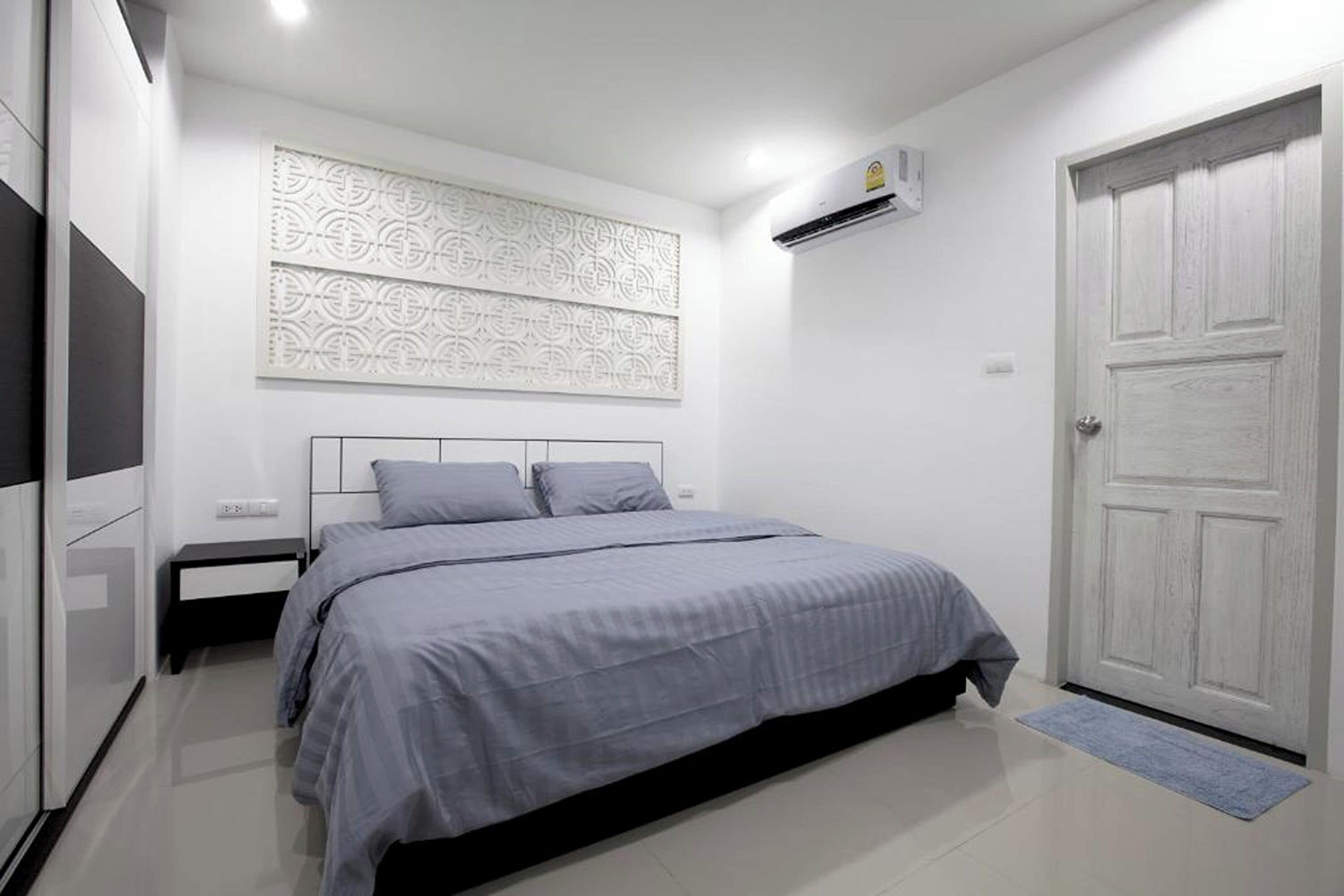 A bedroom with a bed, a nightstand, a wall-mounted air conditioner, and a door.