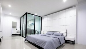 A modern bedroom with a large bed, a glass partition wall, and a white tiled floor. - Number 4 Phuket (Rawai)