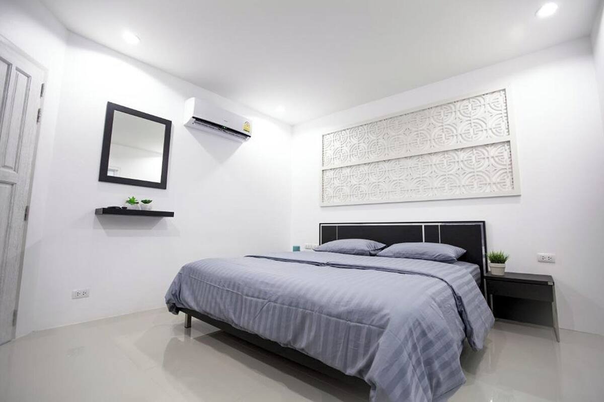 A modern bedroom with a bed, bedside tables, a wall-mounted air conditioner, a mirror, and a decorative panel.