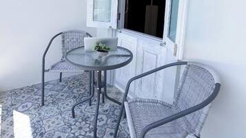 Un pequeño espacio al aire libre con dos sillas y una mesa, piso estampado y una ventana con contraventanas.