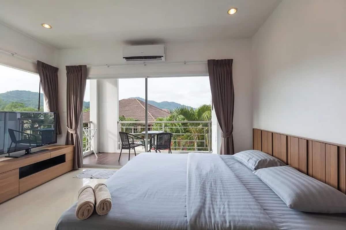 A hotel room with a bed, a TV, a balcony with a table and chairs, and a view of the mountains.