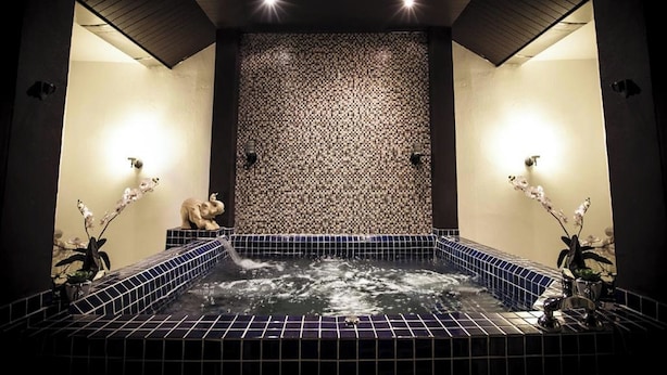 A spa room with a tiled hot tub, two wall-mounted lights, and decorative orchids. - Number 4 Phuket (Rawai)