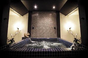A spa room with a tiled hot tub, two wall-mounted lights, and decorative orchids. - Number 4 Phuket (Rawai)