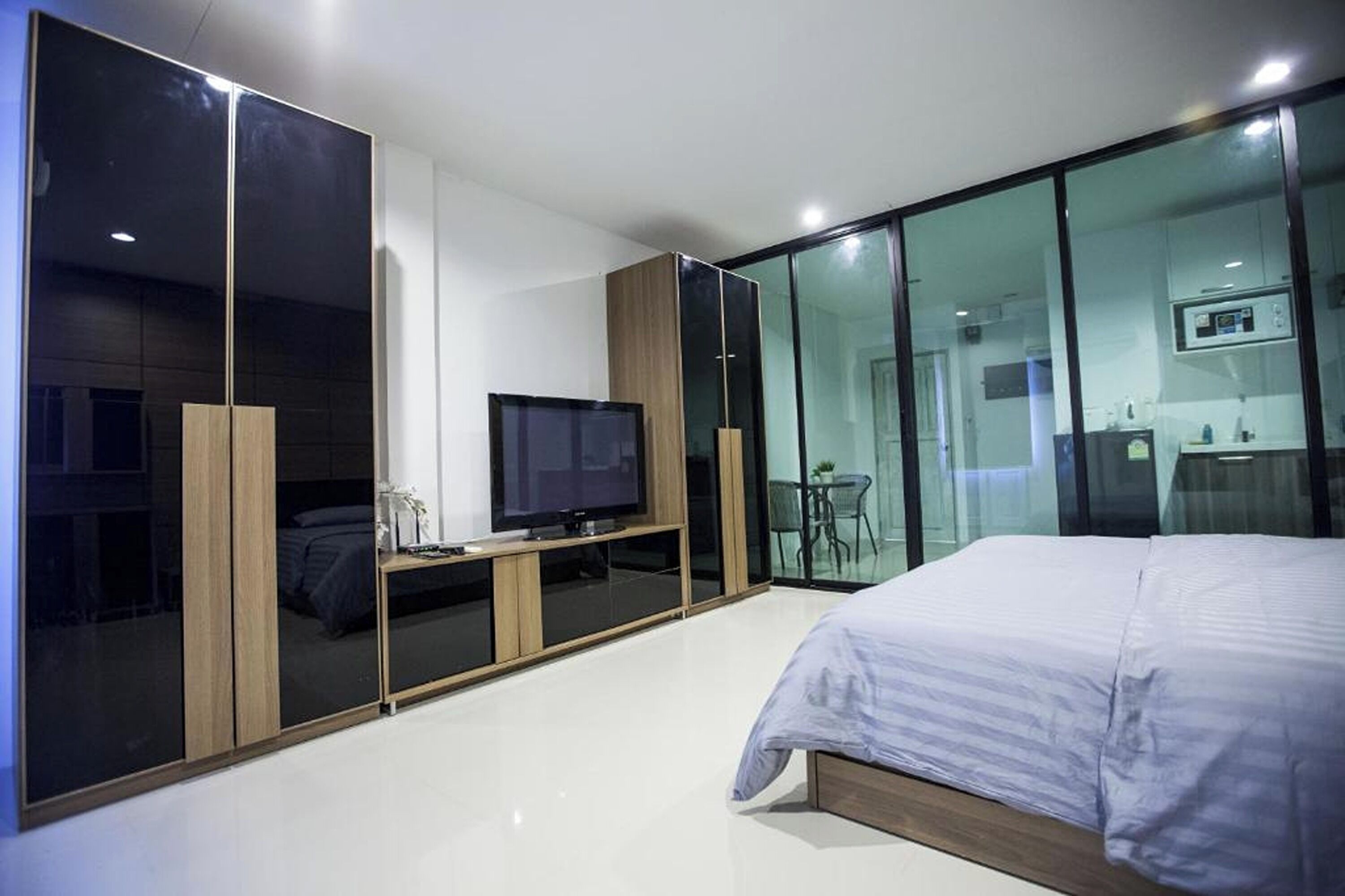 Une chambre moderne avec un grand lit, une télévision et une salle de bain fermée par des parois de verre.