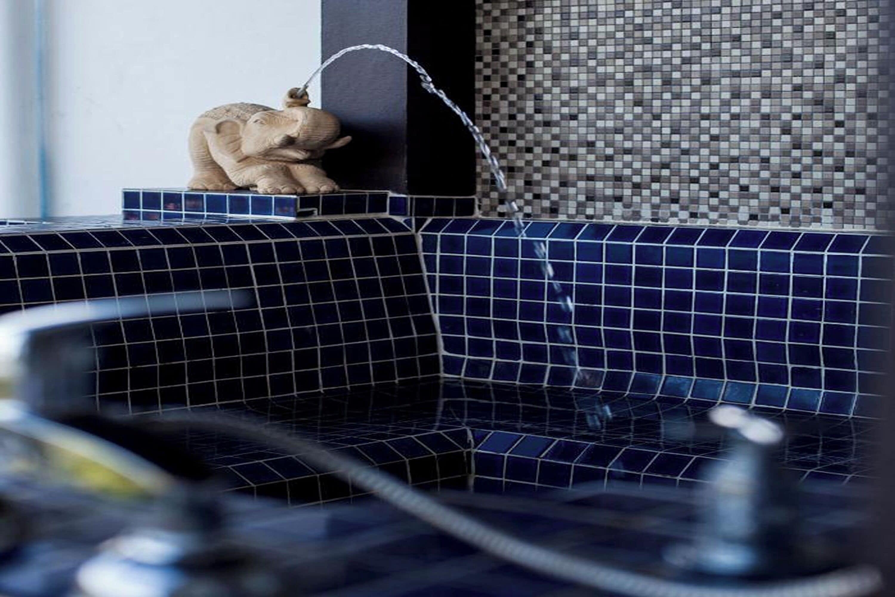 A bathroom with a blue-tiled sink, a small elephant figurine, and a mosaic-patterned wall.
