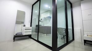 A modern, well-lit room with a glass partition, a bed, a chair, and a kitchenette area. - Number 4 Phuket (Rawai)