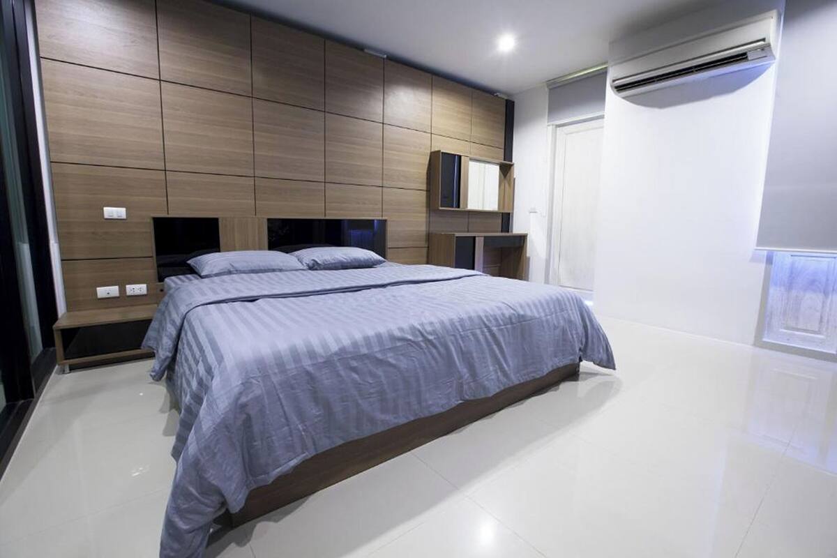 A modern bedroom with a large bed, built-in wooden headboard, and a small desk area.