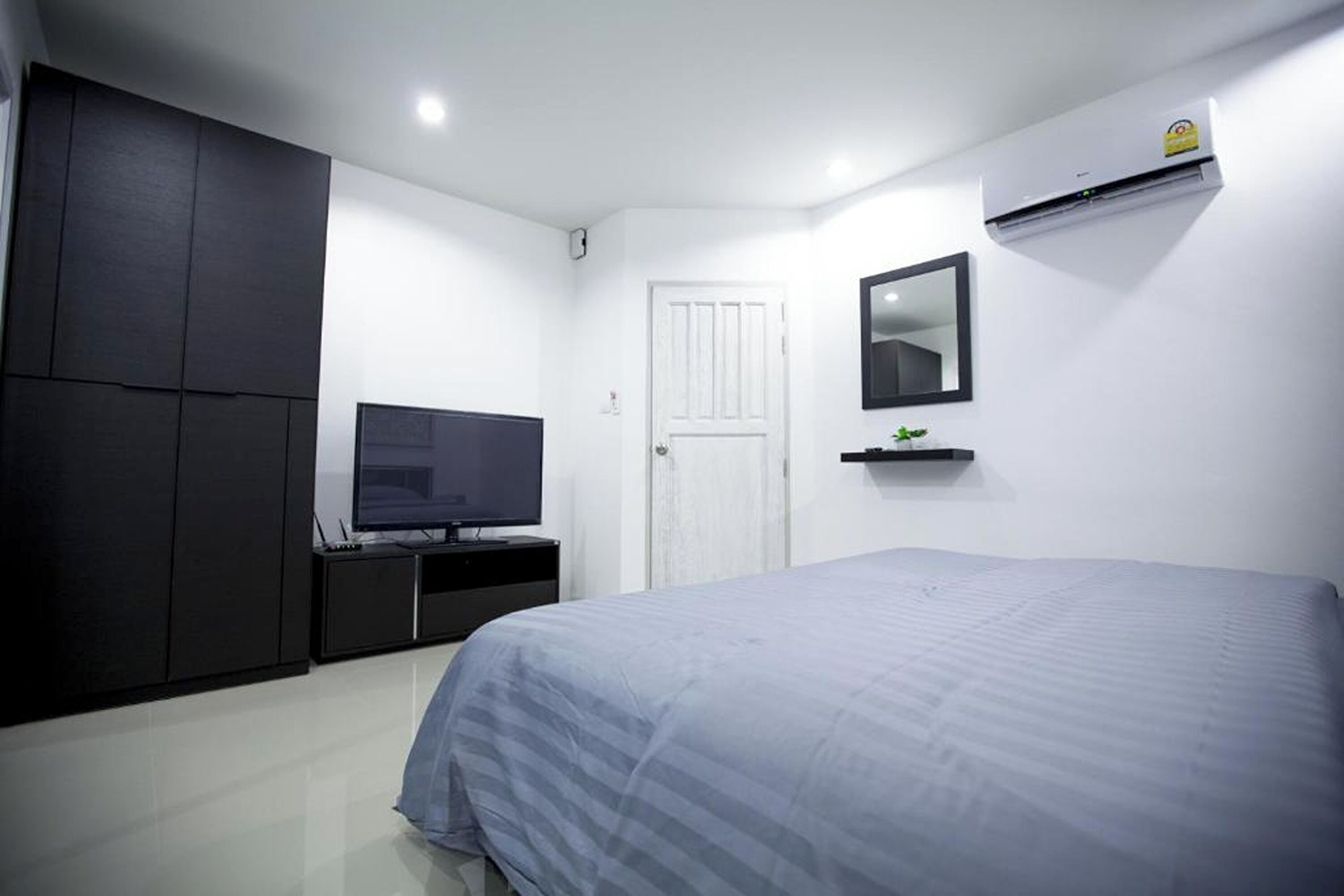 Ein Schlafzimmer mit einem Bett, einem Fernseher auf einem Schrank, einem Kleiderschrank, einer Tür und einer Klimaanlage.