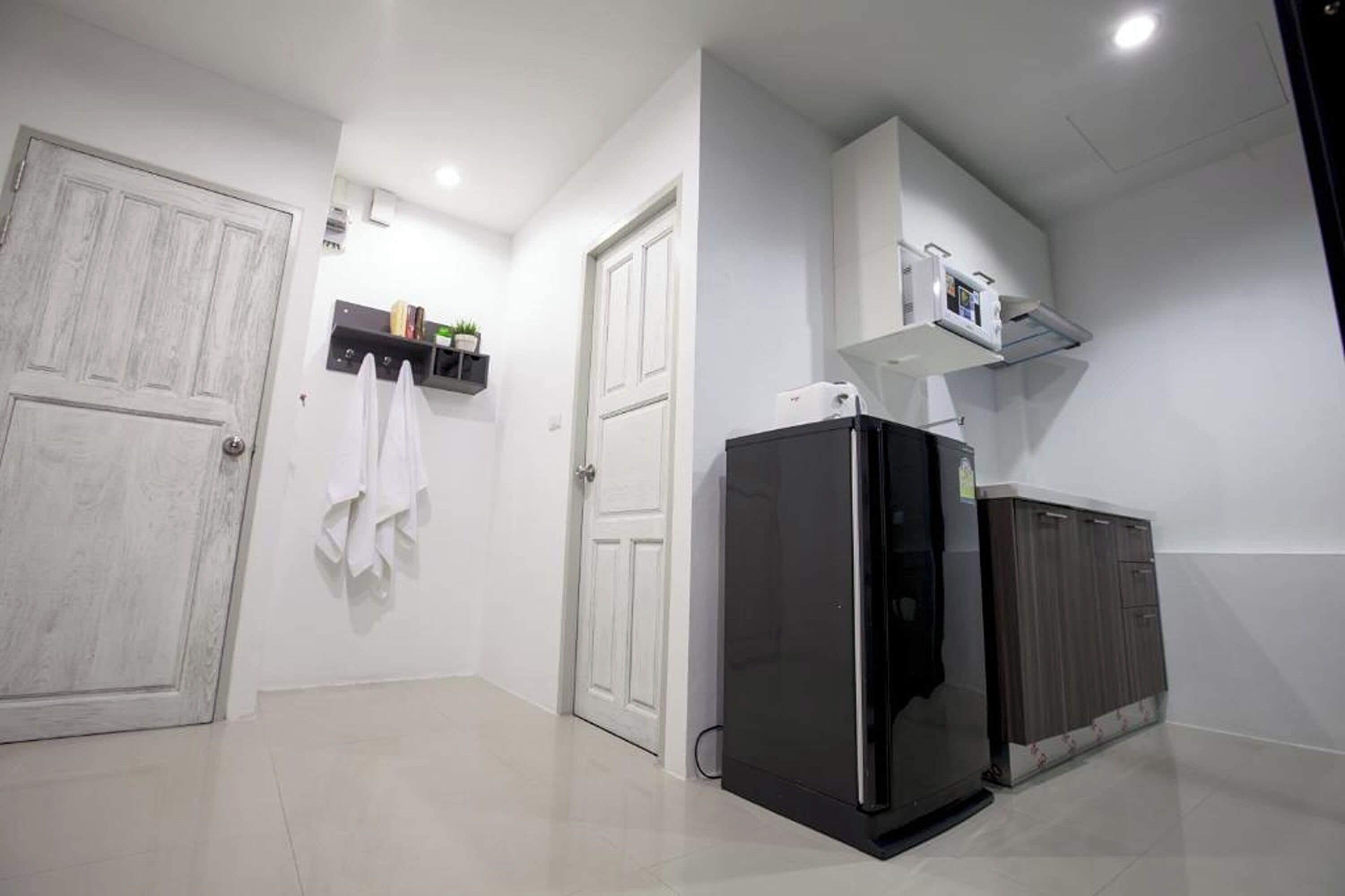 A modern kitchen with a black refrigerator, white cabinets, and a small shelf with books and a plant.