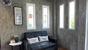 Une pièce avec un canapé en cuir noir, une petite table d’appoint sur laquelle se trouvent un livre et une plante, et une affiche motivante accrochée au mur.