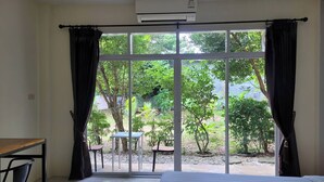 Une chambre avec une grande porte-fenêtre coulissante donnant sur un jardin. On y trouve un lit avec des serviettes pliées, un bureau et deux chaises.