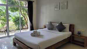 Une chambre avec une grande fenêtre, un lit avec des serviettes pliées, une table de chevet et une petite commode.