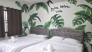 Camera d'albergo con due letti, entrambi con lenzuola e asciugamani bianchi, una testiera grigia rivestita in tessuto e un grande murale con foglie tropicali.