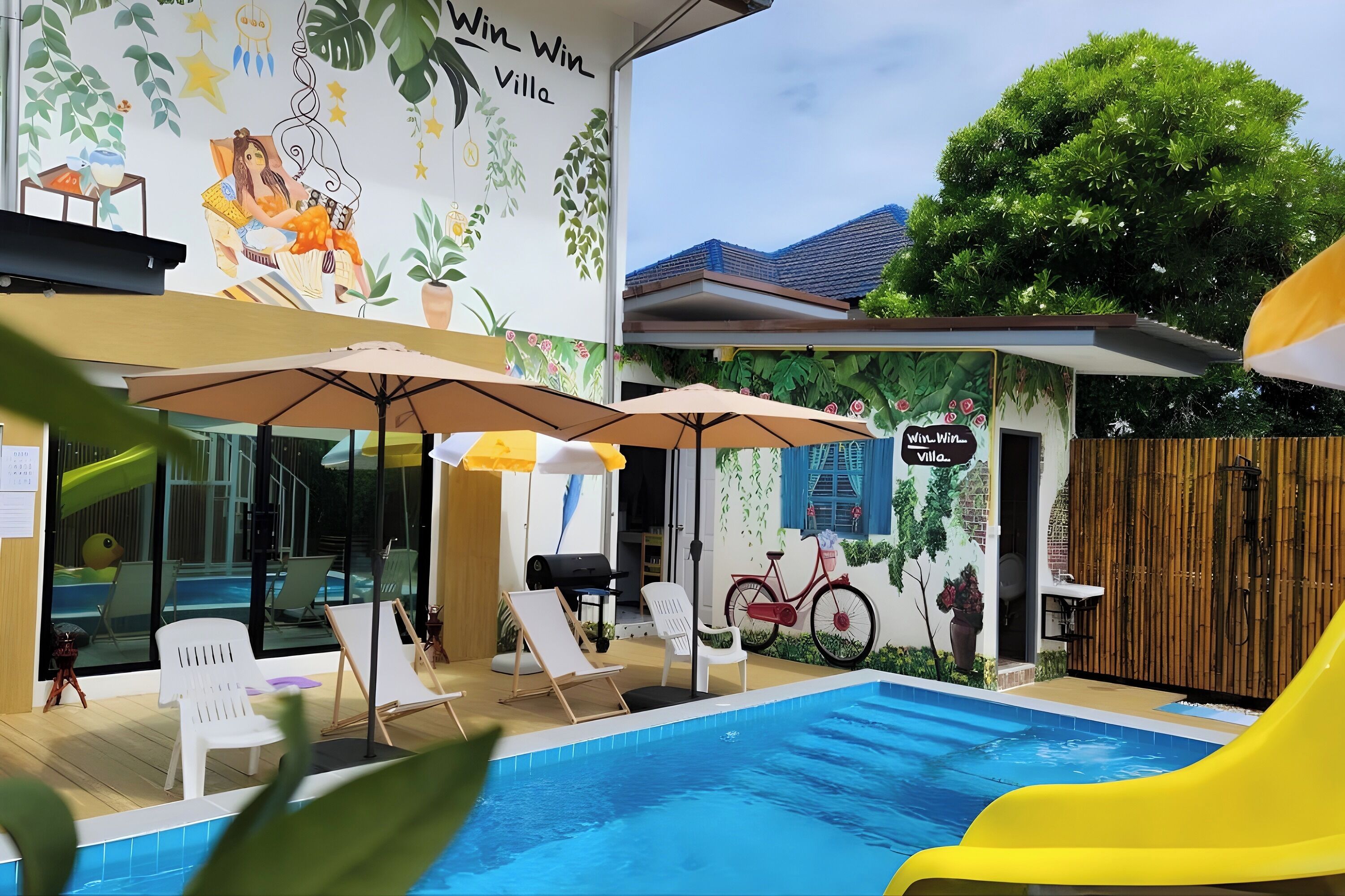 A pool area with lounge chairs and umbrellas, a mural on the wall, and a bicycle.