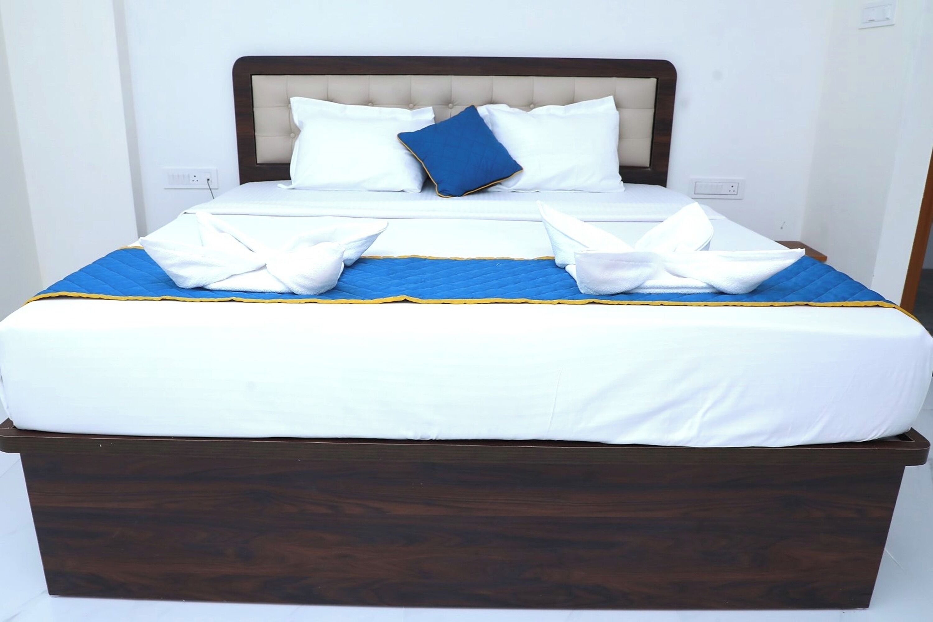 A neatly made bed with white and blue bedding, a wooden headboard, and a blue quilted bedspread.