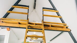 Een stapelbed met een houten trap, een plafondventilator en een muur met behang van tropische bladeren.