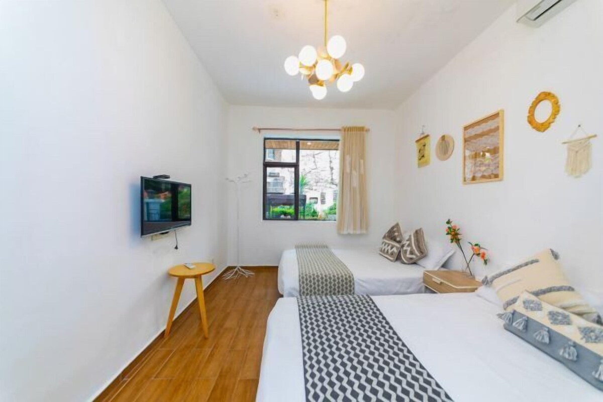 A bedroom with a bed, bedside tables, a TV, a window with curtains, and a chandelier.