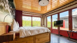 A bedroom with a wooden bed, a TV, and large windows with a view of greenery. - Detached Home in Friesland by Canal (Jistrum / Skûlenboarch)